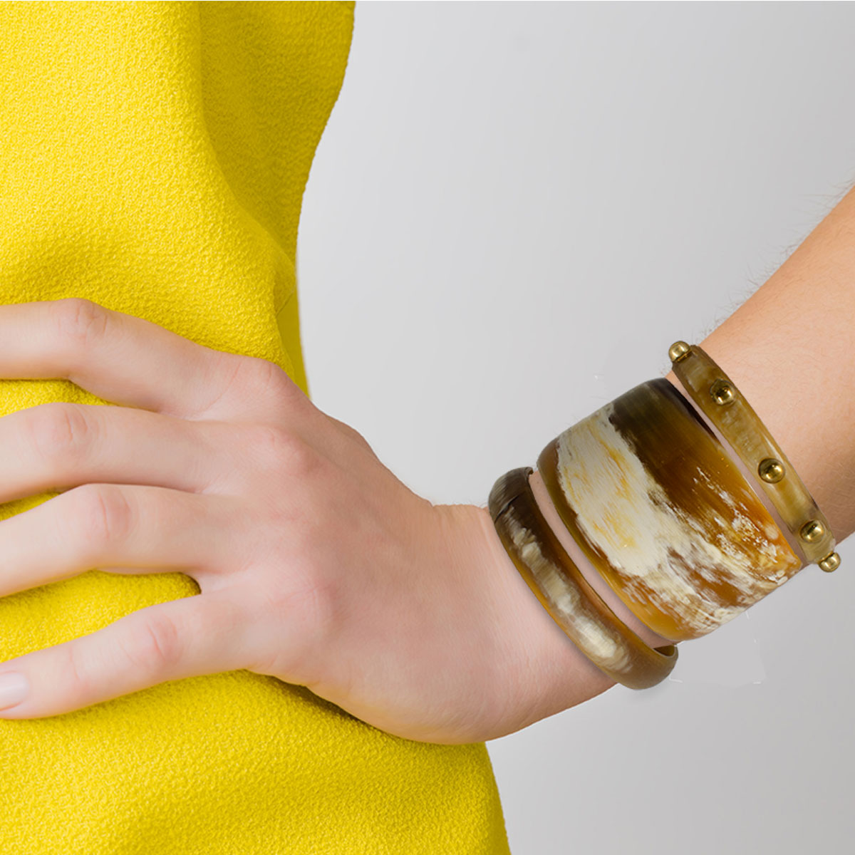 Woman in yellow, bright clothes on gray background. Hand on hip wearing vintage horn stack bracelets