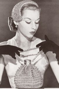 1950s photo of a model in a half hat with a cocktail purse, wearing gloves.