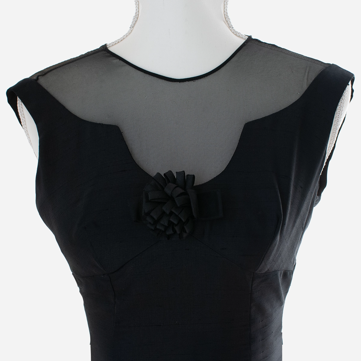 Front close-up: “Close-up of sheer illusion neckline and ribbon rosette on 160s black cocktail dress.
