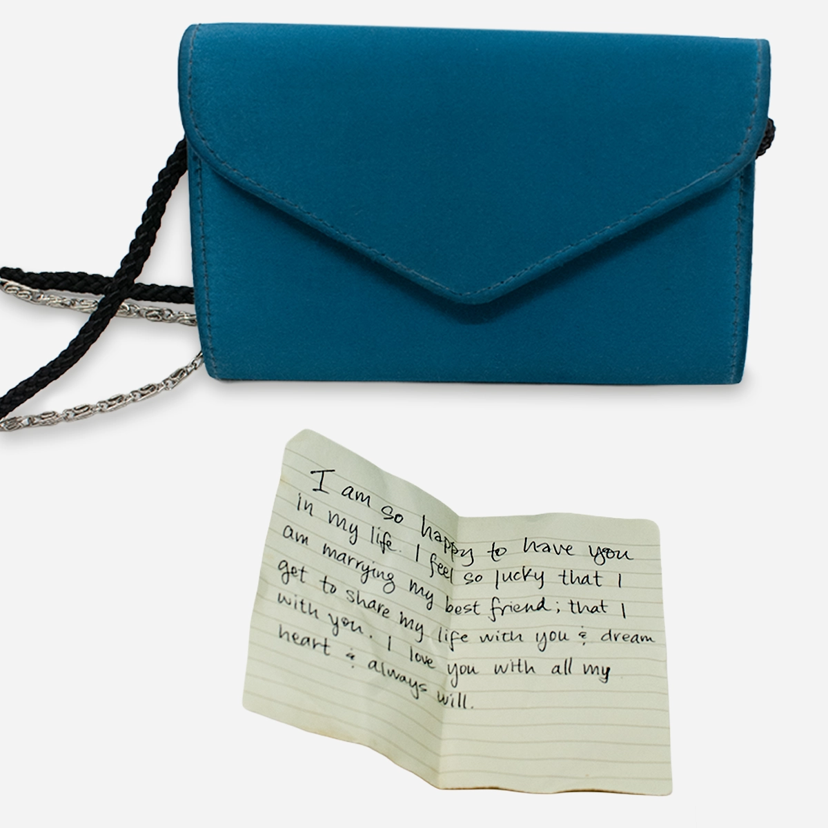 Blue envelope-style evening bag with a handwritten love note displayed beside it.