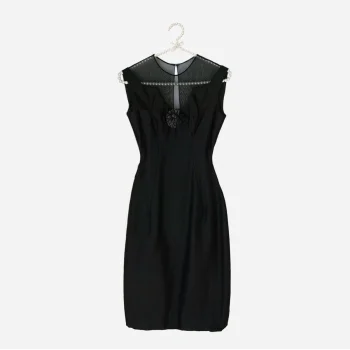 Flat lay on hanger: “1960s black cocktail dress hanging, featuring illusion neckline and fitted shape.”