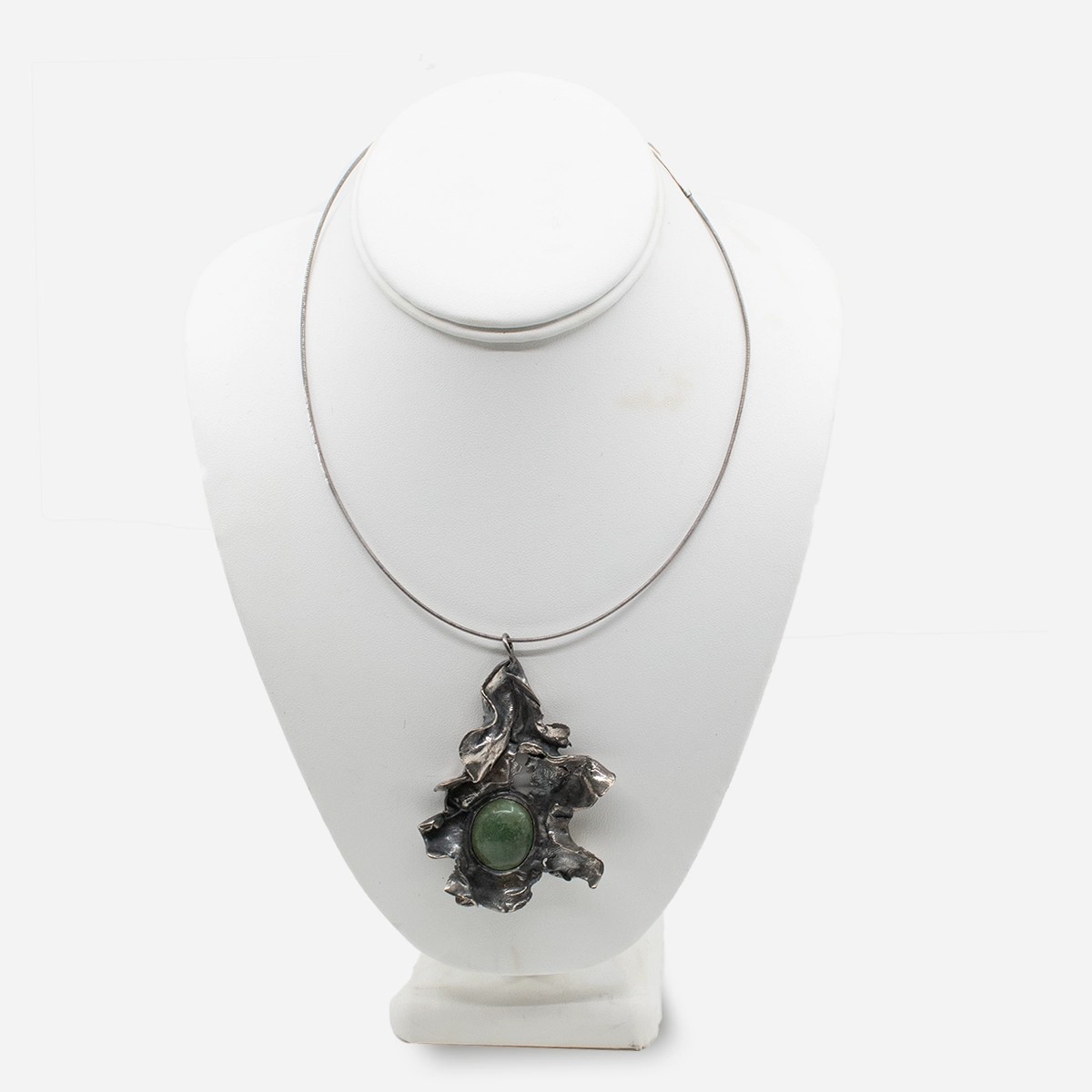 Brutalist silver pendant with green jade cabochon shown on a display bust; pendant hangs from a simple wire necklace not included with the item