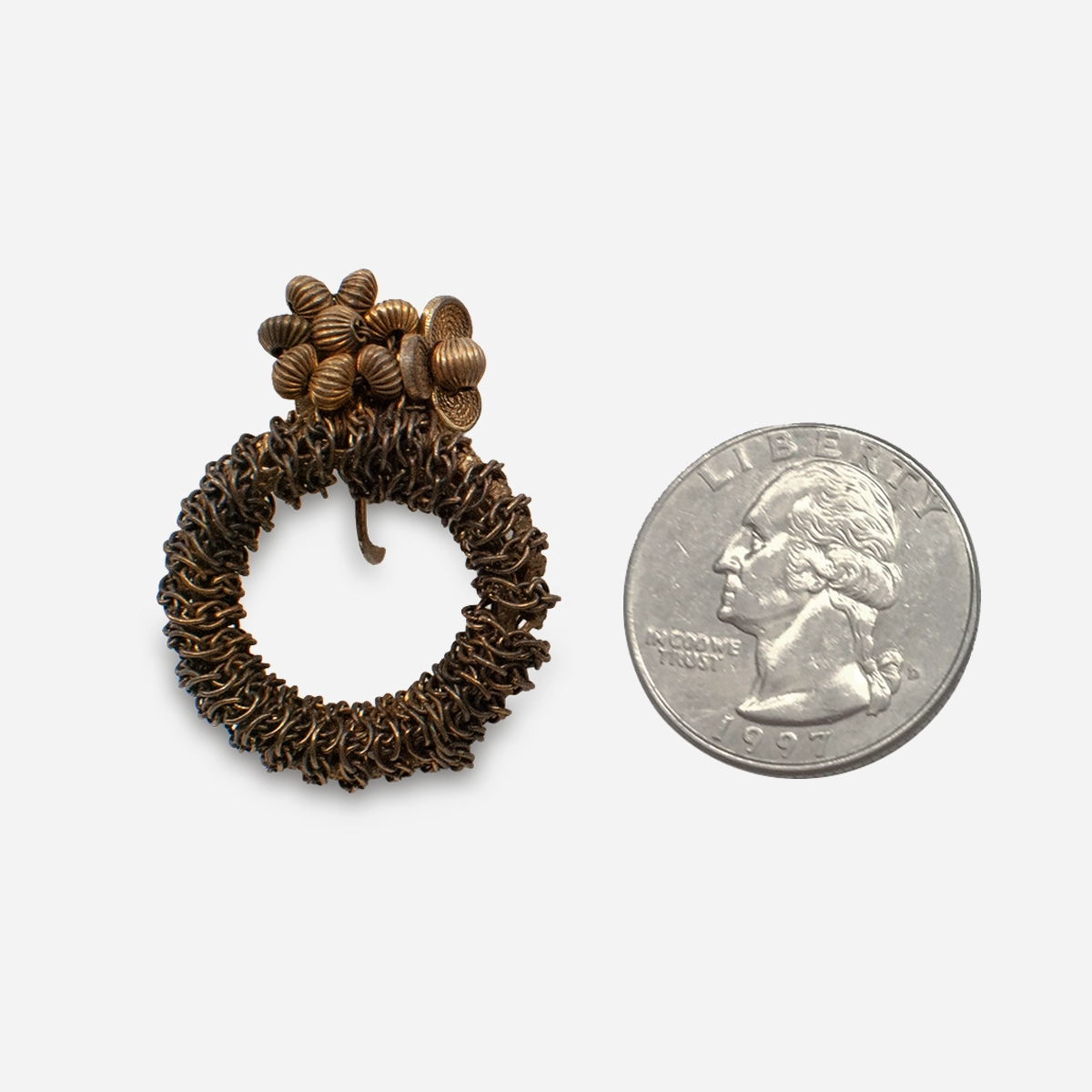 Scale photo of Miriam Haskell brass clip earring shown beside a U.S. quarter
