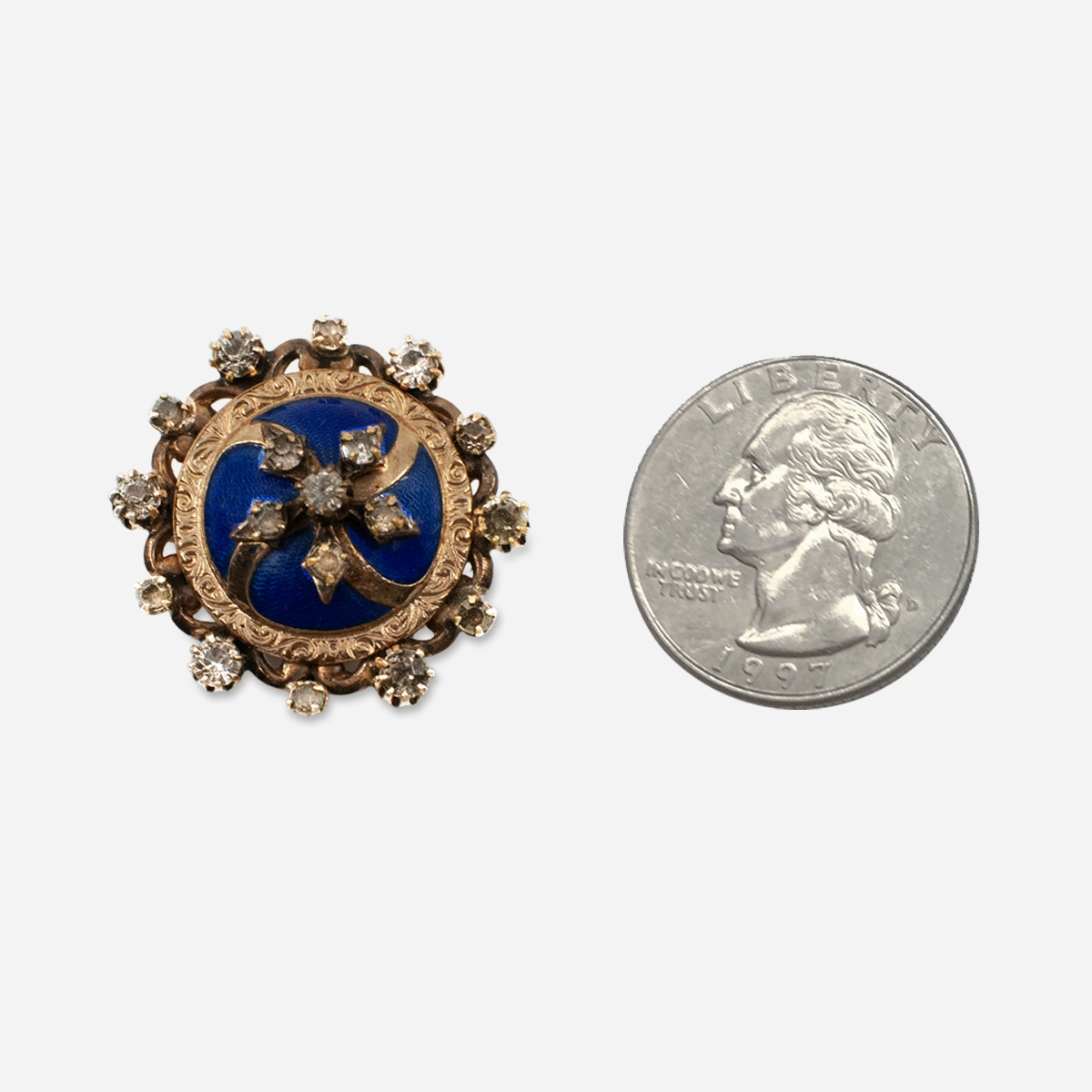 Antique blue enamel brooch beside coin showing approximate 1 inch size