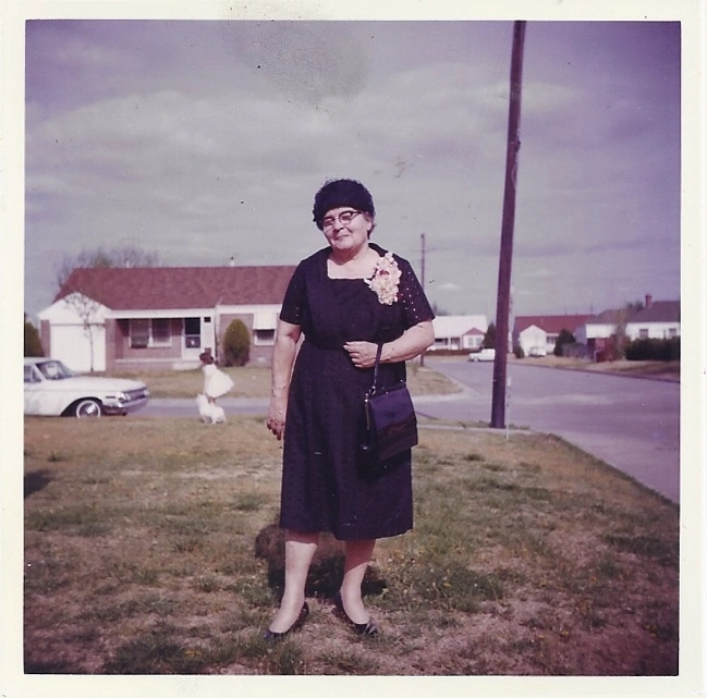Madge in the 1960s wearing a dress and hat, photographed outdoors in a suburban setting.