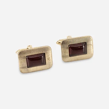 Close-up of 1950s gold-tone cufflinks with textured frames and deep red Lucite-style centers.