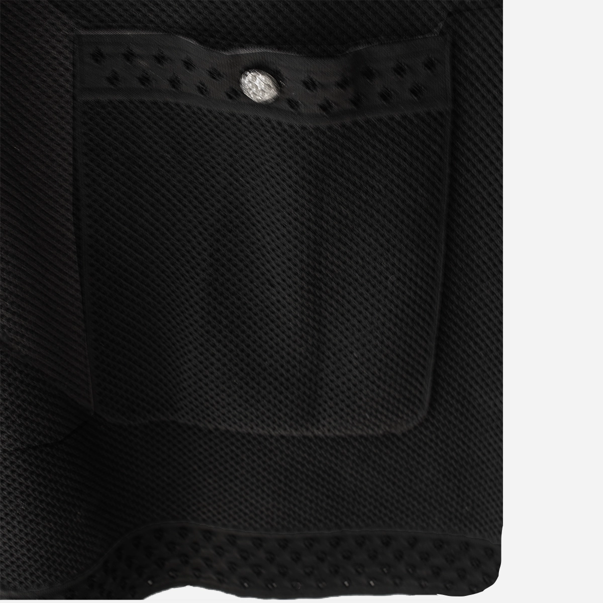 black perforated fabric pocket Close-up of Chanel black textured knit patch pocket with perforated dotted trim and silver-tone logo button.
