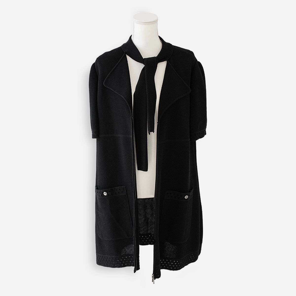 hanel Black Perforated Knit Neck Tie Detail Zip-Front Dress Chanel black perforated knit jacket worn open on dress form with self tie collar hanging loose and front patch pockets visible.