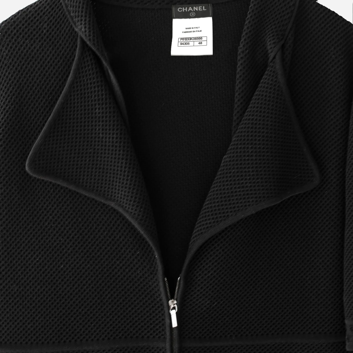 womens double collar jacket Close-up of Chanel black cotton knit jacket neckline showing textured fabric, wide lapel collar, zipper pull, and interior label.